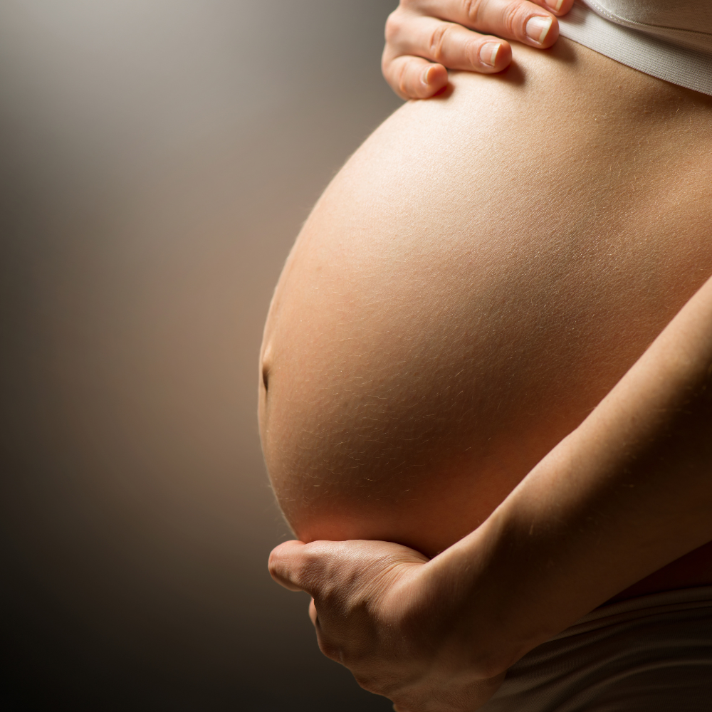 Pregnant belly with floral oil setup, symbolizing nurturing maternity therapy
